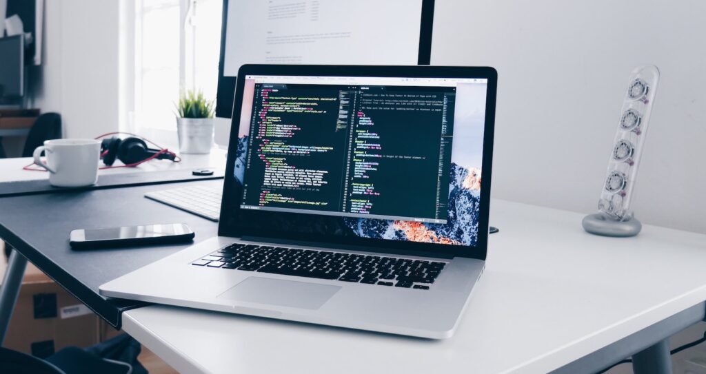 A MacBook with lines of code on its screen on a busy desk